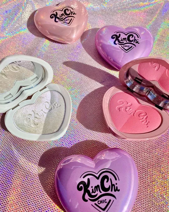 Open pink, purple and white KimChi Chic makeup compacts on a sparkling background.